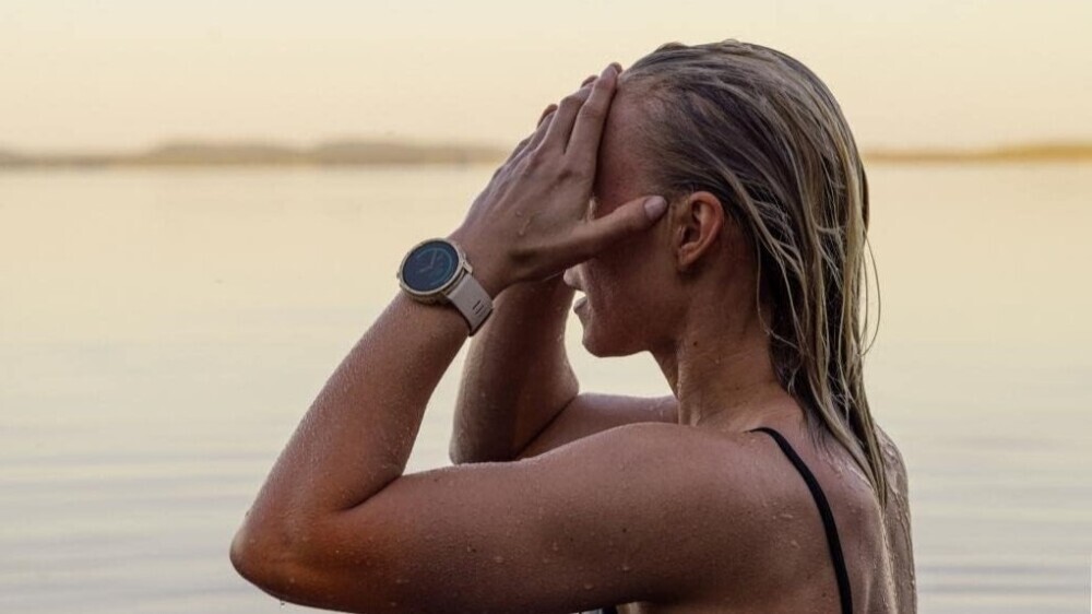 woman wearing smartwatch hands on the head standing by the beach looking ahead