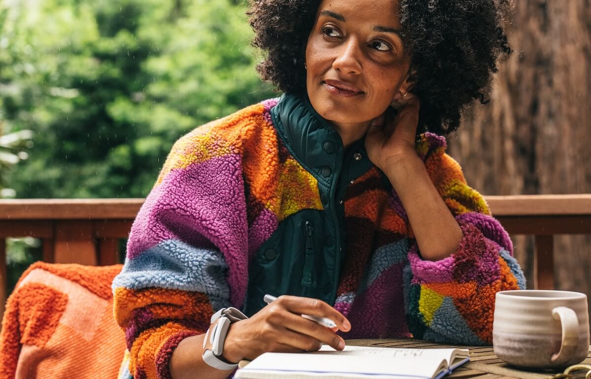Woman wearing Apollo Neuro looking thoughtful and focused as she works at her outdoor workspace with cup of coffee.